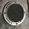 A close-up view of a round ventilation baffle with a metal grate, attached to a gray fabric surface. Produktbild-Vorschau