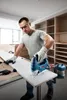 A man is using a jigsaw to cut a piece of wood in a workshop. Anteprima dell’immagine prodotto