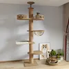 A cat tree is shown in a room with a cat sleeping on a bed at the base of the tree. There are also framed pictures and plants in the background. Produktbild-Vorschau