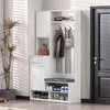 A white entryway organizer with a bench, hooks, and storage compartments, placed next to a door and a plant. Produktbild-Vorschau