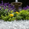 Transparente Glaskristalle als Beetabdeckung vor einer Brunnenfigur und bunten Blumen Produktbild-Vorschau