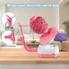 A yarn winder is shown on a wooden table, with several balls of yarn in the background. The product is pink and white. Produktbild-Vorschau