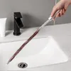 A hand is holding a drain cleaning brush over a white sink. Produktbild-Vorschau