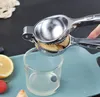A hand is using a manual citrus juicer to squeeze lemon juice into a glass. There are also some fruits like blueberries, tomatoes, and a lemon slice visible on a blue tray. Produktbild-Vorschau