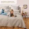 A woman is lying on a bed reading a book, with a quilted bedspread. Anteprima dell’immagine prodotto