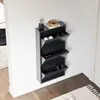 A narrow, dark gray shoe cabinet with three flip-down compartments is mounted on a white wall in a hallway. The cabinet is filled with shoes. A small potted plant and a decorative bowl sit on top of the cabinet. Náhled obrázku produktu