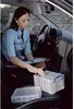 A woman is sitting in the driver's seat of a car, looking at documents and interacting with storage boxes. Náhled obrázku produktu