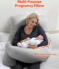 A woman is holding a baby while sitting on a bed with a large pregnancy pillow. Podgląd zdjęcia produktu