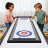 Two children are playing a tabletop curling game in a room. Produktbild-Vorschau
