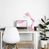A pink desk lamp is on a desk next to a laptop, a mug, and a plant. Anteprima dell’immagine prodotto