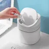 A hand is shown throwing a crumpled tissue into a small white trash can on a desk next to a laptop. Produktbild-Vorschau