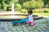 A young girl plays with a toy tractor and trailer in a park near a fountain. Produktbild-Vorschau
