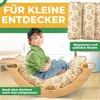 A young boy is sitting on a wooden rocking toy with colorful rainbow and star patterns. The background shows a room with furniture. Produktbild-Vorschau