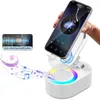 A hand holding a smartphone, which is placed on a white speaker stand with colorful LED lights. Musical notes are depicted emanating from the speaker. Produktbild-Vorschau