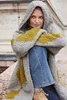 A woman wearing a hooded cardigan and jeans, sitting outdoors. Produktbild-Vorschau