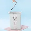 A hand is shown closing the lid of a light gray laundry basket with a woven pattern, which sits on a pink mat against a light blue background. Voir les images du produit
