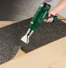 A person is using a green heat gun to peel up a dark, textured material from a wooden surface. Produktbild-Vorschau