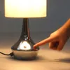 A hand is touching the base of a table lamp. Náhľad obrázku produktu
