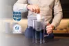 A person is inserting a filter into a glass water pitcher. Produktbild-Vorschau