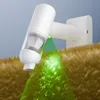 A white handheld vacuum cleaner is shown mounted on a wall charger, with a green light beam illuminating dust particles on a brown fuzzy surface. Produktbild-Vorschau