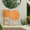 An orange metal bistro set (chair and table) is placed on a gravel patio next to a large succulent plant, with a concrete wall and greenery in the background. Produktbild-Vorschau