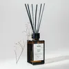 A brown glass diffuser bottle with black reeds and a dried flower stem next to it, set against a plain white background. Náhľad obrázku produktu