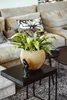 A plant in a gold pot sits on a black side table in front of a sofa. Produktbild-Vorschau