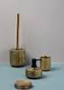 A set of gold-colored bathroom accessories, including a toilet brush holder, soap dispenser, and cup, arranged on a light blue surface against a light gray background. Náhled obrázku produktu