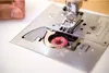 A close-up view of a sewing machine's bobbin area with thread. Produktbild-Vorschau