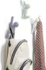 Three decorative hooks shaped like climbing figures are mounted on a white wall. One hook holds a backpack, and another holds a scarf. Náhled obrázku produktu