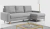 A light gray sectional sofa with wooden legs is shown against a white background. A floor lamp is visible in the background.