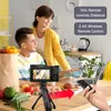 A couple is in a kitchen, with a camera set up on a tripod. There are groceries and food items on the counter. Produktbild-Vorschau