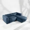 A blue sectional sofa is displayed on a white platform with shadows on the wall behind it. Produktbild-Vorschau