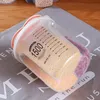 A clear plastic food storage container with markings for volume, filled with grains and beans, placed on a grey cloth. Produktbild-Vorschau