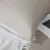 A close-up of a taupe striped pillowcase with a white textured throw blanket and a book partially visible. Podgląd zdjęcia produktu