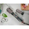 A hair styling tool with interchangeable brush heads is displayed on a marble surface, alongside a small plant and decorative items. Náhľad obrázku produktu