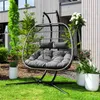 A hanging chair with cushions is placed on a green lawn in front of a modern house with wooden siding. Produktbild-Vorschau