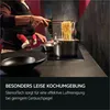 A person is cooking pasta in a kitchen while holding a baby in a carrier. Produktbild-Vorschau