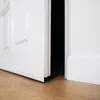 A close-up view of a white door and its baseboard, with a sliver of darkness visible in the gap between the door and the frame. Anteprima dell’immagine prodotto