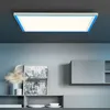 A modern LED panel light with a blue frame is mounted on a dark gray ceiling above a shelf with decorative items and framed artwork. Produktbild-Vorschau