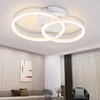 A modern white LED ceiling light with two interlocking rings, mounted on a white ceiling in a living room setting. Podgląd zdjęcia produktu