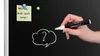 A hand holding a chalk marker is about to draw a question mark in a speech bubble on a black magnetic board. A sticky note with holiday information is attached to the board. Produktbild-Vorschau