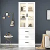 A white display cabinet with glass doors and drawers, filled with books and decorative items. It's placed in a room with a dark blue wall and a small side table. Podgląd zdjęcia produktu