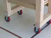 Close-up of the base of a wooden utility cart with casters on a light-colored floor. Voir les images du produit