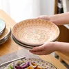 Hands holding a stack of decorative plates with a patterned design. Náhled obrázku produktu