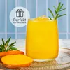 A glass of yellow drink with ice and a rosemary sprig, next to sliced carrots and a whole carrot, on a decorative tray. Produktbild-Vorschau