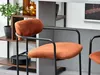 A close-up view of an orange bar stool with a black metal frame, placed in a modern interior setting. Náhľad obrázku produktu