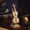 A wooden model of a cello on a stand, placed on a wooden surface with books and other decorative items in the background. Anteprima dell’immagine prodotto
