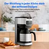 A coffee maker is shown on a wooden table with a croissant and a mug in a kitchen setting. Produktbild-Vorschau