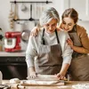 Two women in a kitchen, one older and one younger, are preparing dough. The younger woman has her arm around the older woman's shoulders, and they are both smiling. A red stand mixer is visible in the background. Produktbild-Vorschau